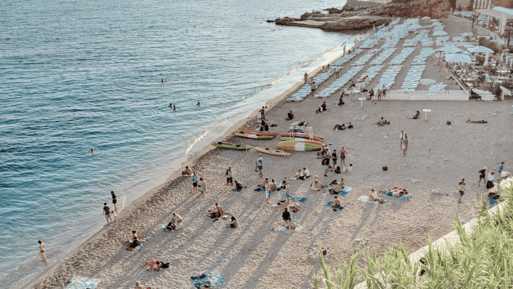 Beach along Dubrovnik’s Adriatic coast with clear blue water, sun loungers and visitors enjoying the shoreline in Croatia.